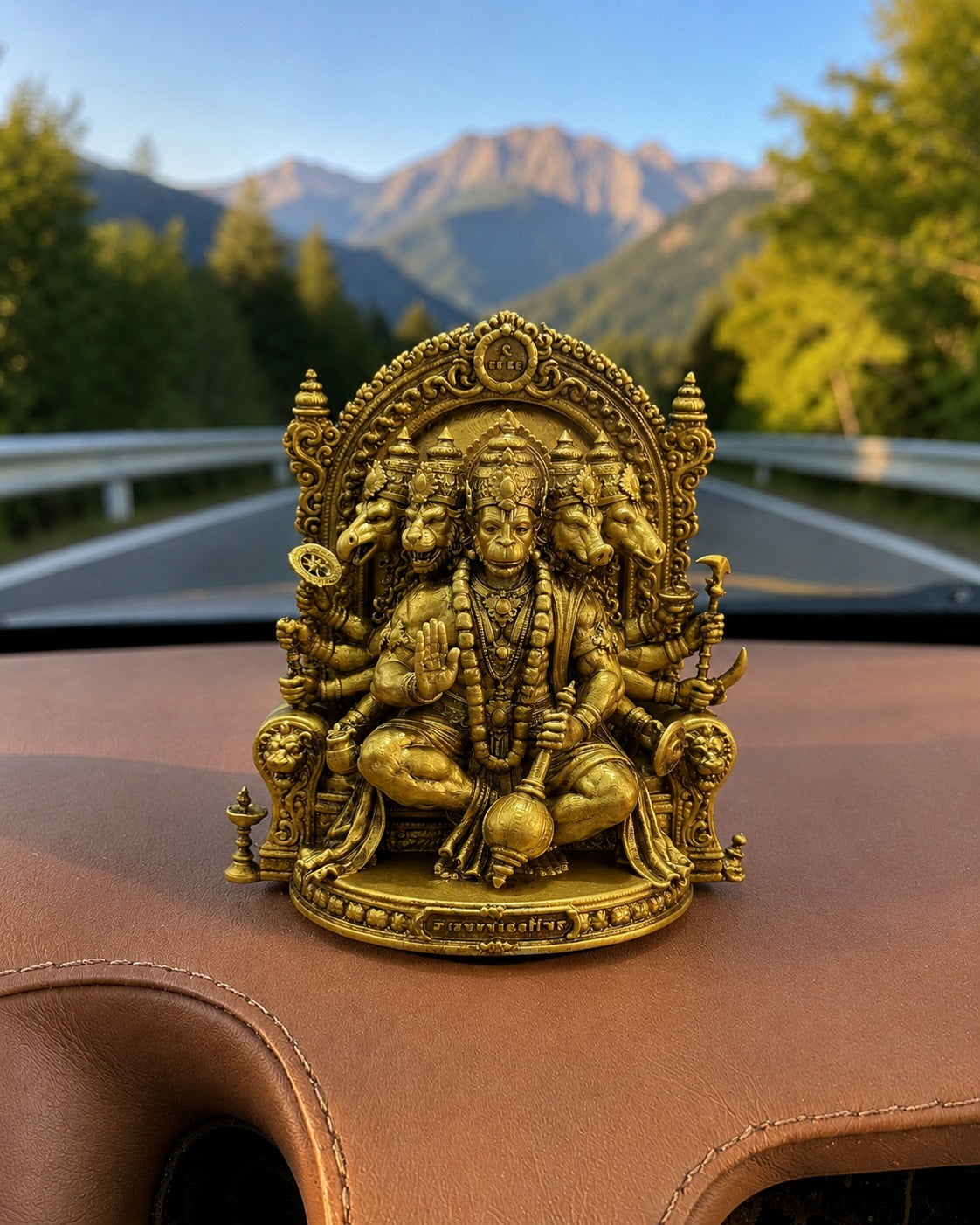 Gold-colored statue of a deity on a car's dashboard with a mountainous landscape in the background