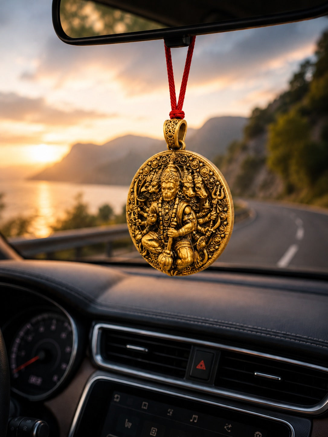 Gold pendant hanging from a car's rearview mirror with a scenic road in the background